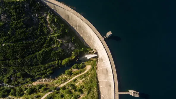 aerial photo of dam: water flows out the left into a green valley, water stored on the right side