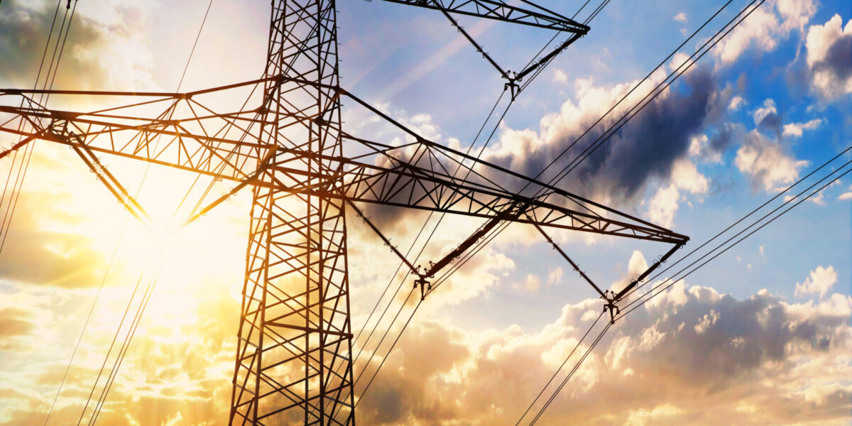 upshot photo electricity pylon / transmission tower against a blue sky with clouds; sun flare on the right