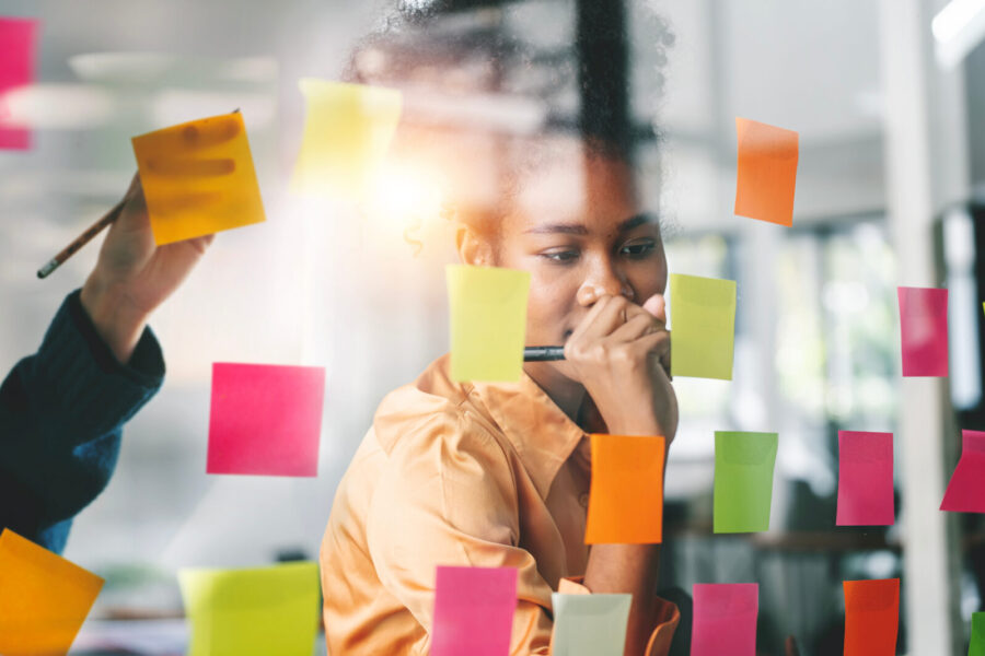 Young woman concentrates & writes note on one of many post-its during brainstorming activity