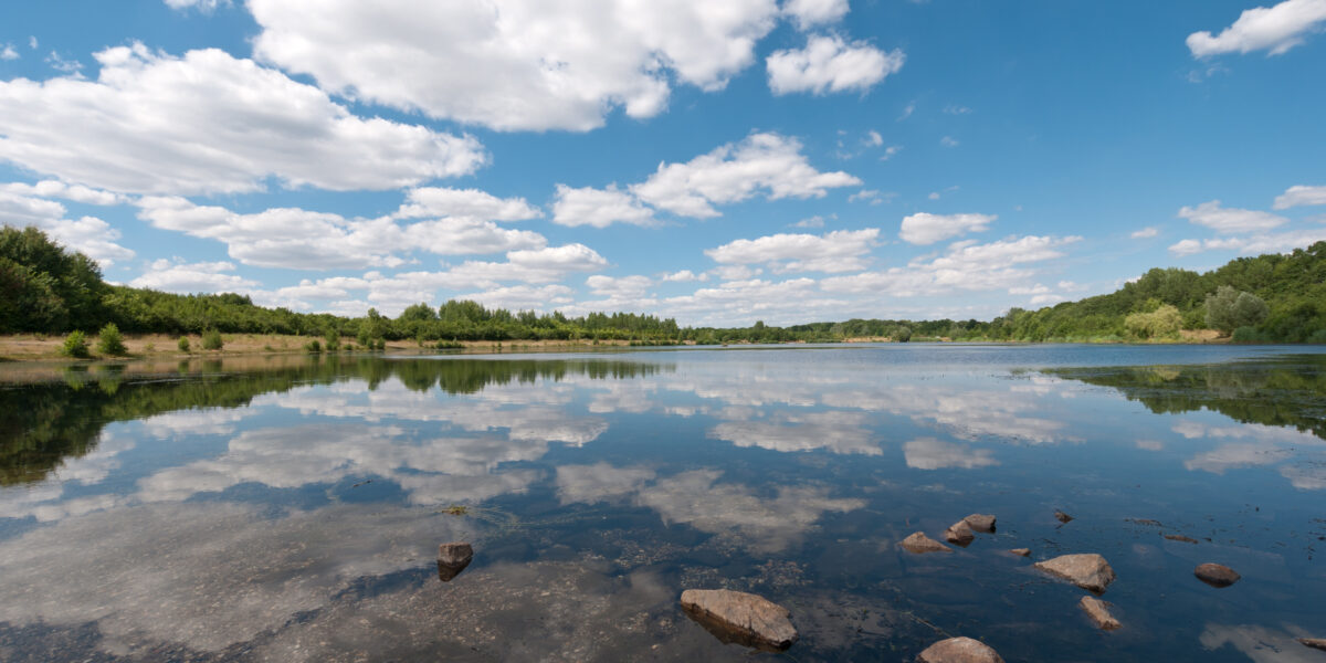 photo white clouds in a blue sky over a green forest and blue lake