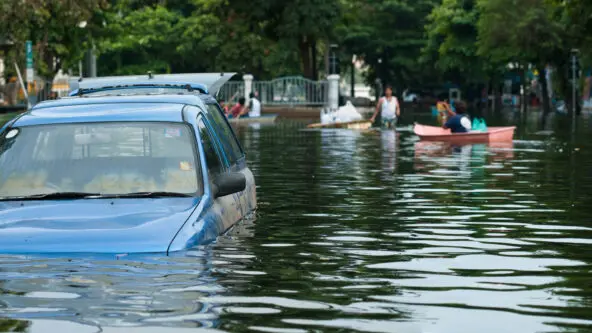 flood water submerges parked car in foreground; survivors in rowboats in background