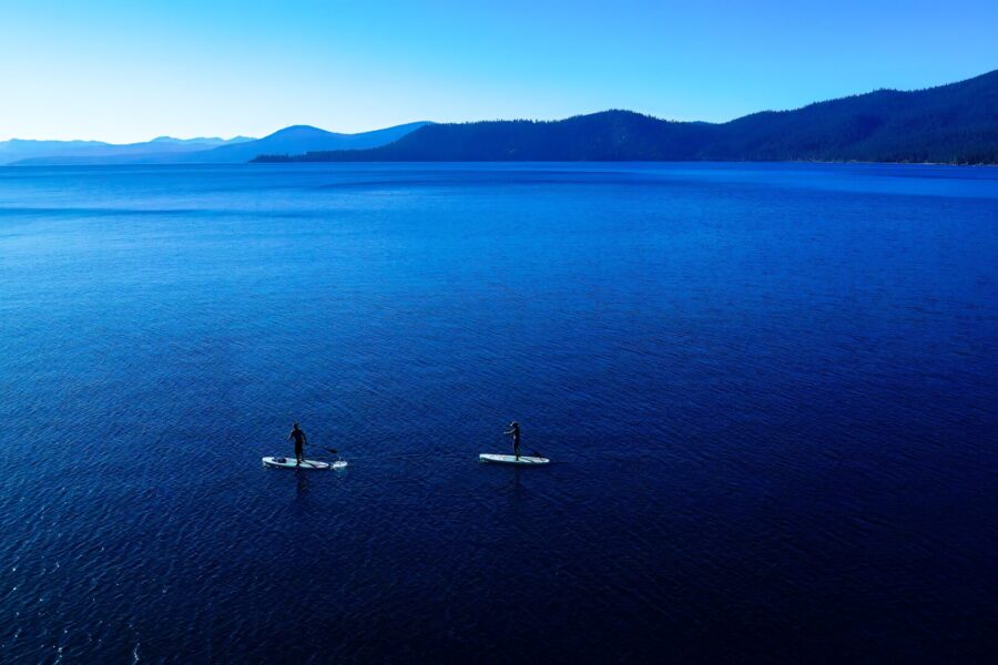 photo of blue Lake Tahoe water with stand-up paddleboarders in the foreground and mountains in the background, source Roland Schumann via unsplash