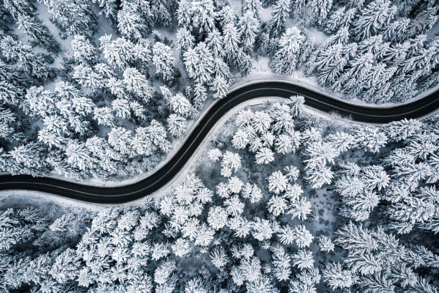 aerial photo clean road curves through a snow-covered forest | source AdobeStock