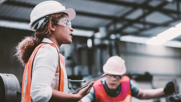 female engineer in hard hat holds tablet while inspecting water facility; water operator in background