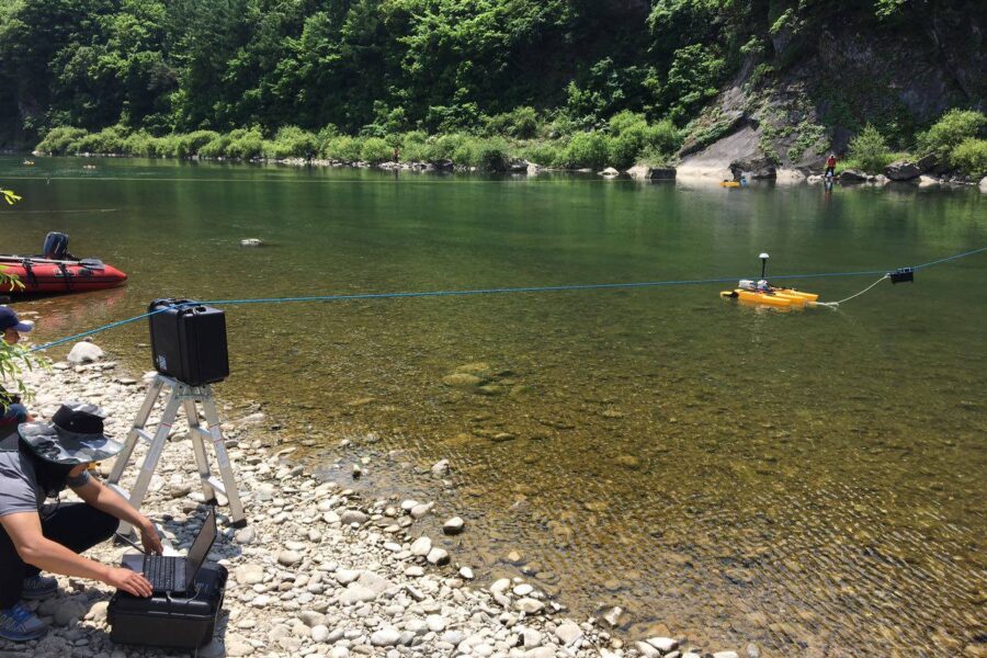 photo of the Flying Fox portable ADCP towing system towing an acoustic Doppler current profiler (ADCP) on a river | hydrographer using a laptop on the bank