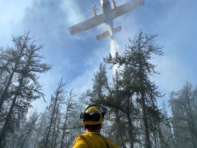 photo Manitoba Wildfire Service crew leader watches aircraft deliver a water drop 